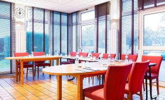 a conference room with several red chairs arranged in a circle around a wooden table at Comfort Hotel Montlucon