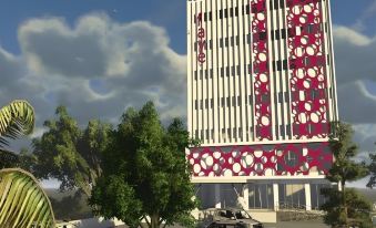 a tall building with a pink and white facade is surrounded by trees and parked cars at favehotel Rembang