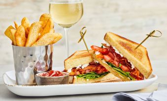 a dining table with a plate of food , including a sandwich and french fries , accompanied by a glass of white wine at Courtyard Toledo Airport Holland