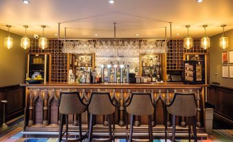 a modern bar with wooden stools , crystal glasses , and various bottles on shelves , as well as a large mirror above the counter at Banchory Lodge Hotel