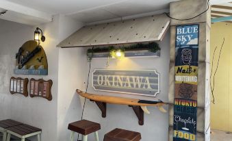 a surfboard and a wooden sign are displayed on a shelf in front of stools at Sunset Beach Hotel