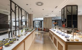 a large , well - lit dining room with a long buffet table filled with various dishes and utensils at NH Leipzig Zentrum