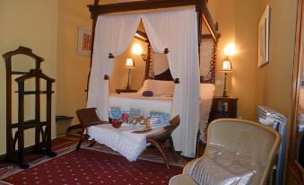 a bedroom with a canopy bed , white canopy , and red carpet , accompanied by chairs and a table at Balneario de Corconte