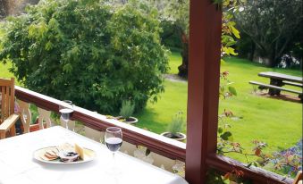 a dining table with a plate of food and a glass of wine on it , situated on a balcony overlooking a lush green lawn at Cambridge House Breakfast & Bed