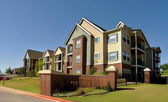 a row of apartment buildings with green grass and red bushes in front , under a clear blue sky at Corse Lawn House Hotel