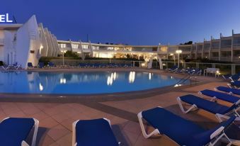 a large swimming pool with blue lounge chairs and a building in the background at night at Hotel Zodiaco