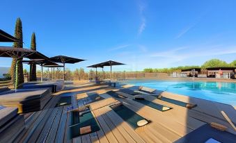 a large outdoor pool surrounded by a wooden deck , with several lounge chairs and umbrellas placed around the pool area at Torre de Palma Wine Hotel, Montforte, a Member of Design Hotels