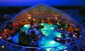 an indoor swimming pool with a large glass dome roof , surrounded by people enjoying their time in the water at Akzent Hotel Aufkirchen