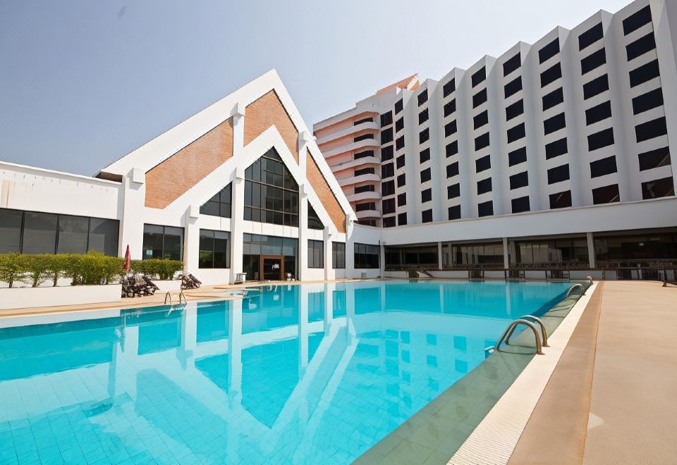 a large , modern swimming pool with a white building and black windows in the background at Rimpao Hotel