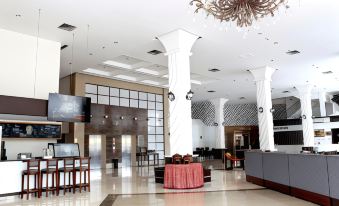 a spacious lobby with white columns , a chandelier , and a red table in the center at Forbis Hotel