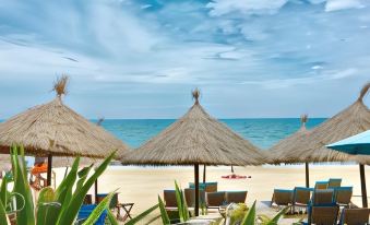 a beach scene with several thatched umbrellas and lounge chairs , providing shade and comfort for beachgoers at Pink Beach Homestay