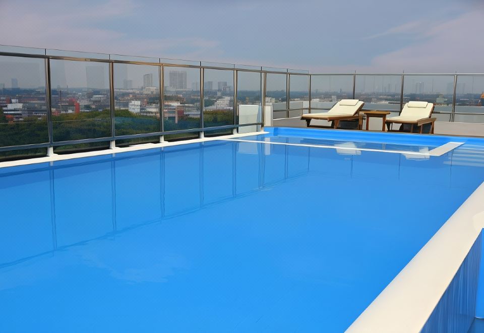 a large blue swimming pool on a rooftop , surrounded by chairs and a view of the city at Pakons Prime Hotel