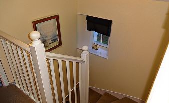 a staircase with a white railing leads to a window and an archway , with a painting hanging on the wall at Hillside