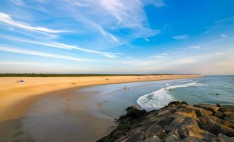 a sandy beach with people walking along the shore , enjoying the sunny day and the blue ocean at AquaHotel