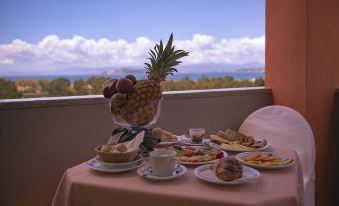 a table is set with various breakfast items , including fruit and pastries , in front of a window overlooking the ocean at Hotel Califfo