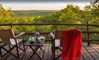 a wooden deck with two chairs and a table set up for a meal , overlooking a beautiful landscape at Elewana Tarangire Treetops