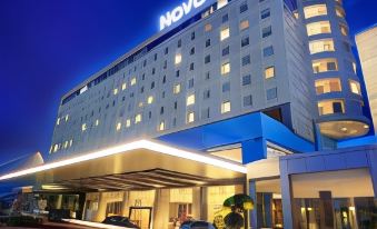 "a large hotel building with the name "" novotel "" on it , surrounded by trees and other buildings at night" at Novotel Bangka - Hotel & Convention Centre