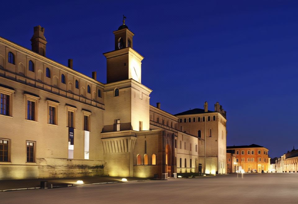 a large building with a clock tower is lit up at night , casting a shadow on the ground at Hotel Touring