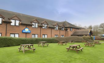 a brick building with a blue sign is surrounded by a green lawn and several picnic tables at Days Inn by Wyndham Sevenoaks Clacket Lane