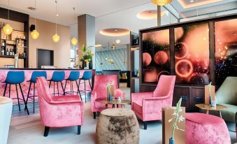 a modern lounge area with pink chairs , a wooden coffee table , and various decorative items at Leonardo Offenbach Frankfurt