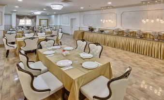 a large dining room with white tables and chairs , gold tablecloths , and multiple menus on display at Royal Hotel