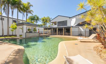 a large swimming pool is surrounded by a building with palm trees and lounge chairs at Coral Cay Resort