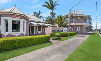 a house with a pink exterior and a green lawn in front of it , surrounded by palm trees at Shellharbour Village Motel