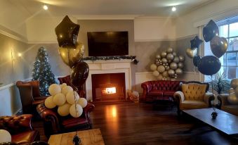 a living room with a fireplace , couches , and a christmas tree decorated with gold and black balloons at Blue Bell Hotel