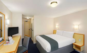 a hotel room with a large bed , a desk , a chair , and a tv . also a door in the room at Days Inn by Wyndham Sutton Scotney South