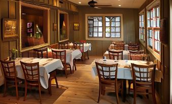 a well - lit dining room with wooden floors , tables covered in white tablecloths , and chairs arranged for guests at Lake Rabun Hotel