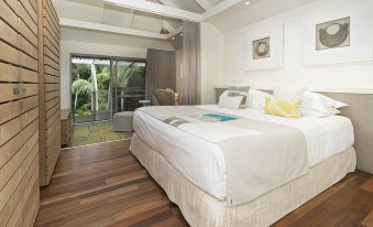 a large bed with white linens is situated in a room with wooden floors and a sliding glass door at Arajilla Retreat