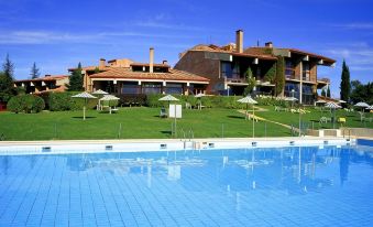 a large swimming pool is in front of a resort with green grass and umbrellas at Parador de Santo Estevo