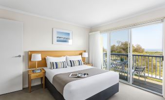 a hotel room with a large bed , a balcony overlooking a golf course , and a book on the bedside table at Quest Williamstown North