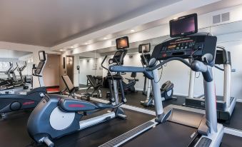 a well - equipped gym with various exercise equipment , including treadmills and ellipticals , along with a television mounted on the wall at The Kenilworth