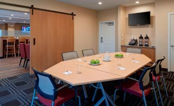 a conference room with a wooden table , blue chairs , and a tv mounted on the wall at TownePlace Suites Grand Rapids Airport