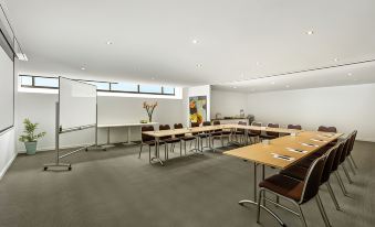 a large conference room with rows of chairs arranged in a semicircle , and a projector screen mounted on the wall at Quest Brighton on the Bay