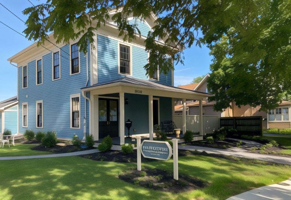 a blue house with a white sign on the front , surrounded by green grass and trees at The Plainfield Inn