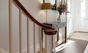 a white staircase with a wooden handrail , leading to a hallway with a vase of flowers on the landing at A Room with A View