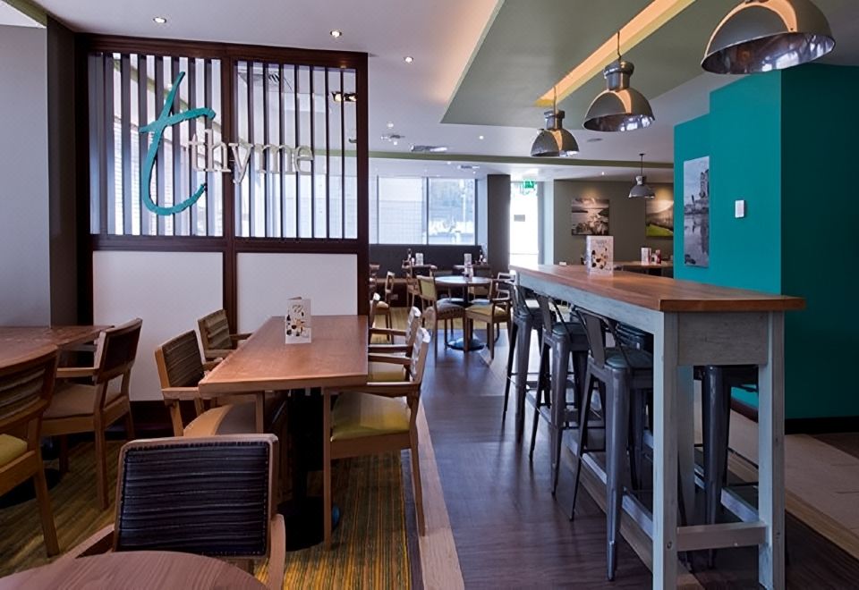 a restaurant with wooden tables and chairs , a bar area , and hanging lights on the ceiling at Premier Inn Oban