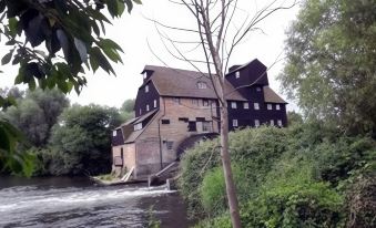 a large brick building is situated near a river , with trees and bushes surrounding it at Three Horseshoes Inn