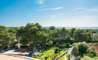 a beautiful outdoor area with green trees , grass , and buildings , set against the backdrop of a sunny blue sky at Hotel Cala Murada