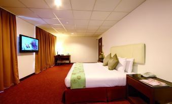 a large bed with a red headboard and white sheets is in a room with a tv on the wall at Jewels Hotel