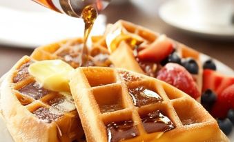 a plate of waffles topped with syrup , fruit , and maple syrup is being poured over at Country Inn & Suites by Radisson, Ashland - Hanover, VA