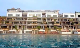 a modern , multi - story building with balconies and greenery , situated near a clear blue swimming pool at Cikidang Plantation Resort