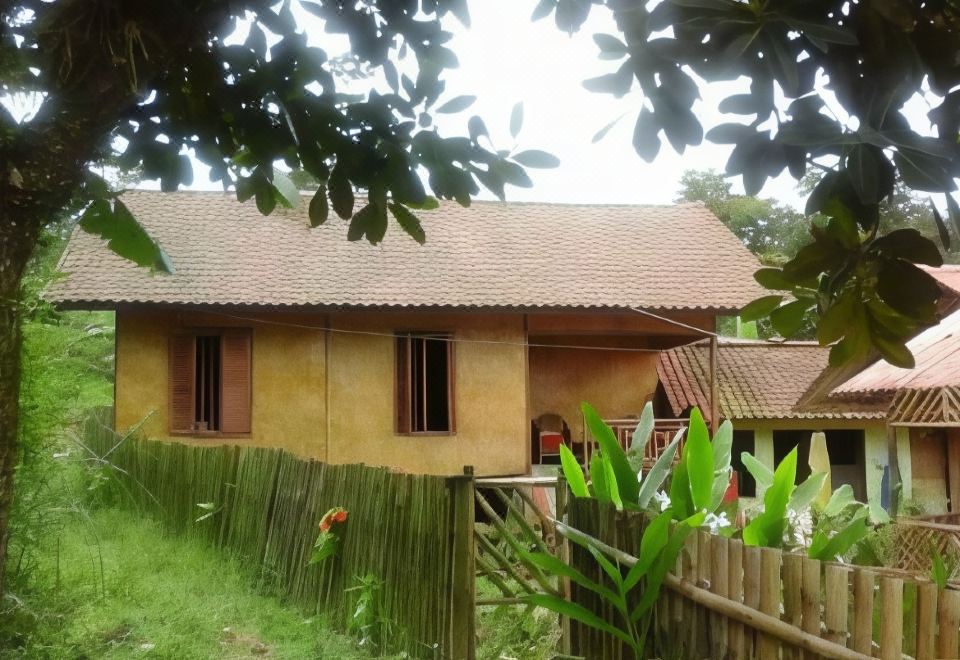 a yellow house surrounded by a wooden fence and lush greenery , with a bamboo fence in front at De Salak Homestay