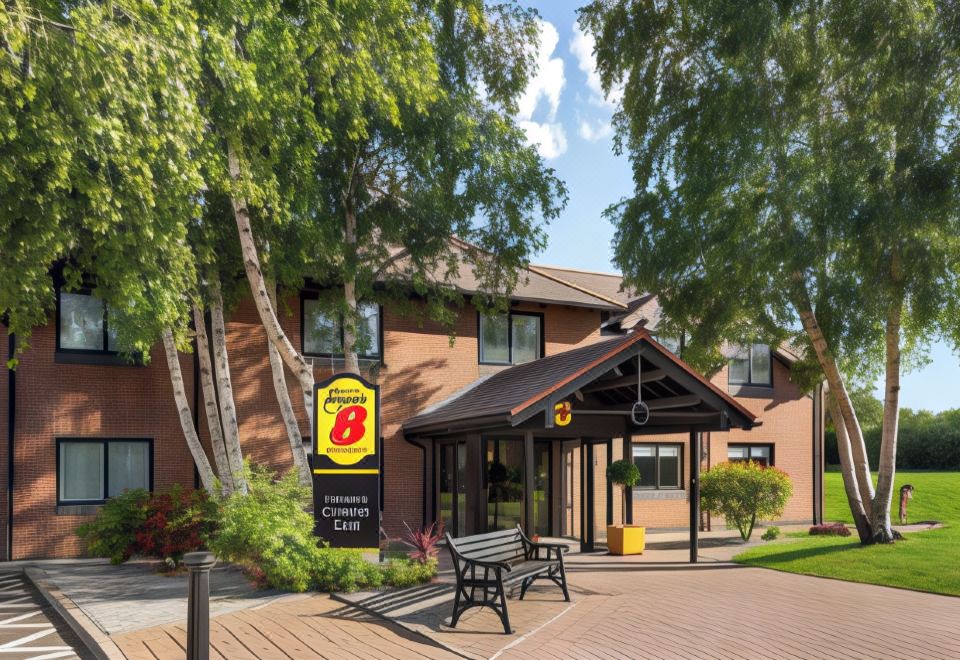 "a hotel entrance with a sign reading "" super 8 "" and a park - like setting featuring benches , trees , and a covered walkway" at Super 8 by Wyndham Chester East