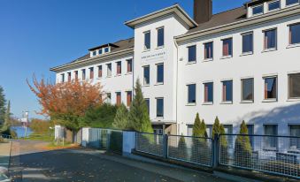 a white building with a red roof , surrounded by trees and other buildings in the background at Hotel am Rhein