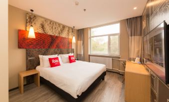 a large bed with white linens and two red pillows is in a room with a window at Ibis Hotel