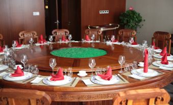 a round wooden dining table with multiple place settings , including wine glasses , plates , and napkins at Spring Hotel