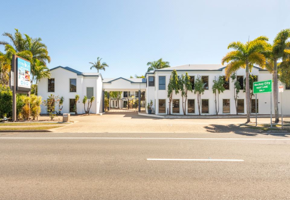 a white building with palm trees and a clear blue sky in front of it at Coral Cay Resort